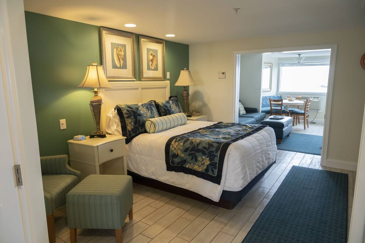 Une chambre d’hôtel comprenant un lit, des tables de chevet, une chaise, un bureau et un balcon avec une table et des chaises.