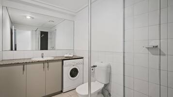 A modern bathroom with a glass shower enclosure, a built-in washing machine, and a toilet.