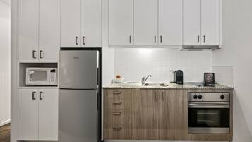 Cocina moderna con armarios blancos, un refrigerador de acero inoxidable, microondas, pileta y horno doble.