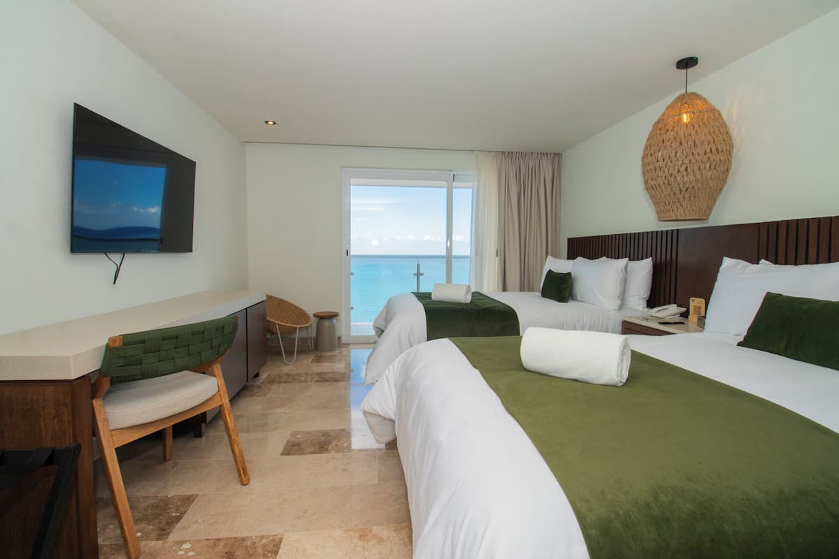 Habitación de hotel con cama, escritorio, silla, televisión y vista al océano.