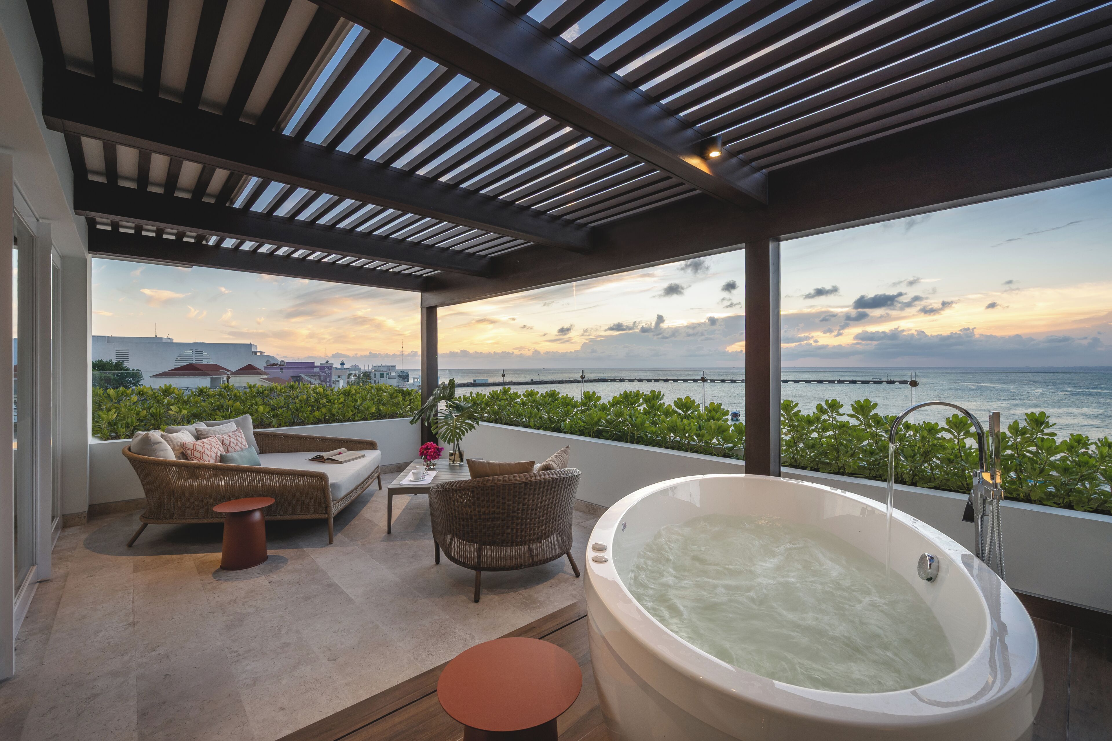 A modern outdoor living area with a large bathtub, wicker furniture, and a view of the sea.