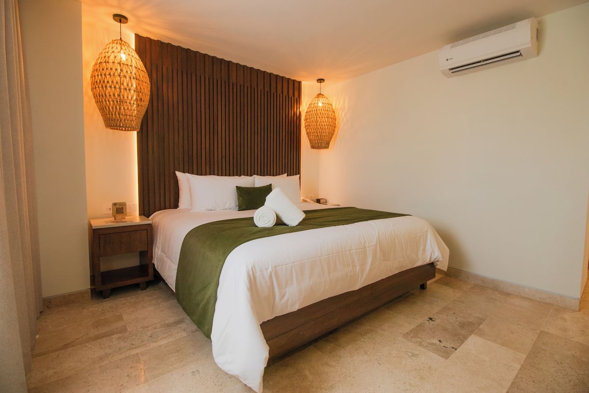 Una habitación de hotel con una cama, mesitas de noche, aire acondicionado de pared y dos lámparas colgantes.