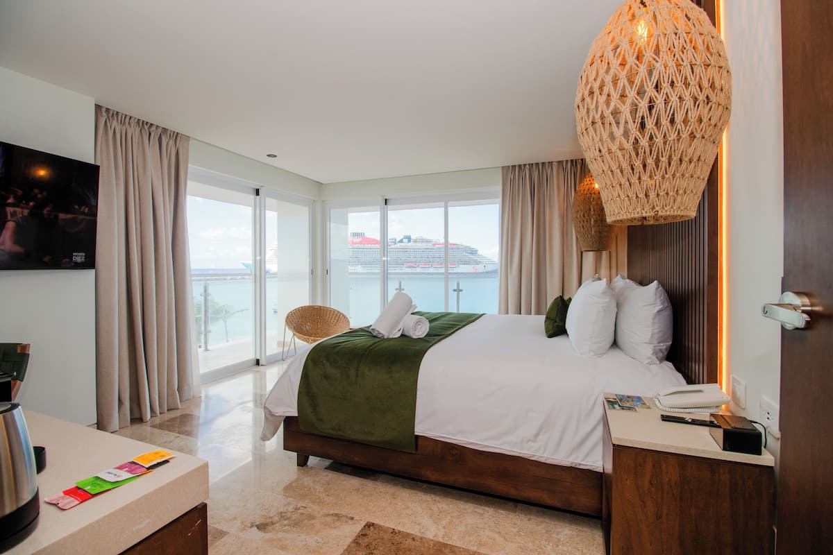 Habitación de hotel moderna con una cama grande, televisión, escritorio con cafetera y vista a un crucero.