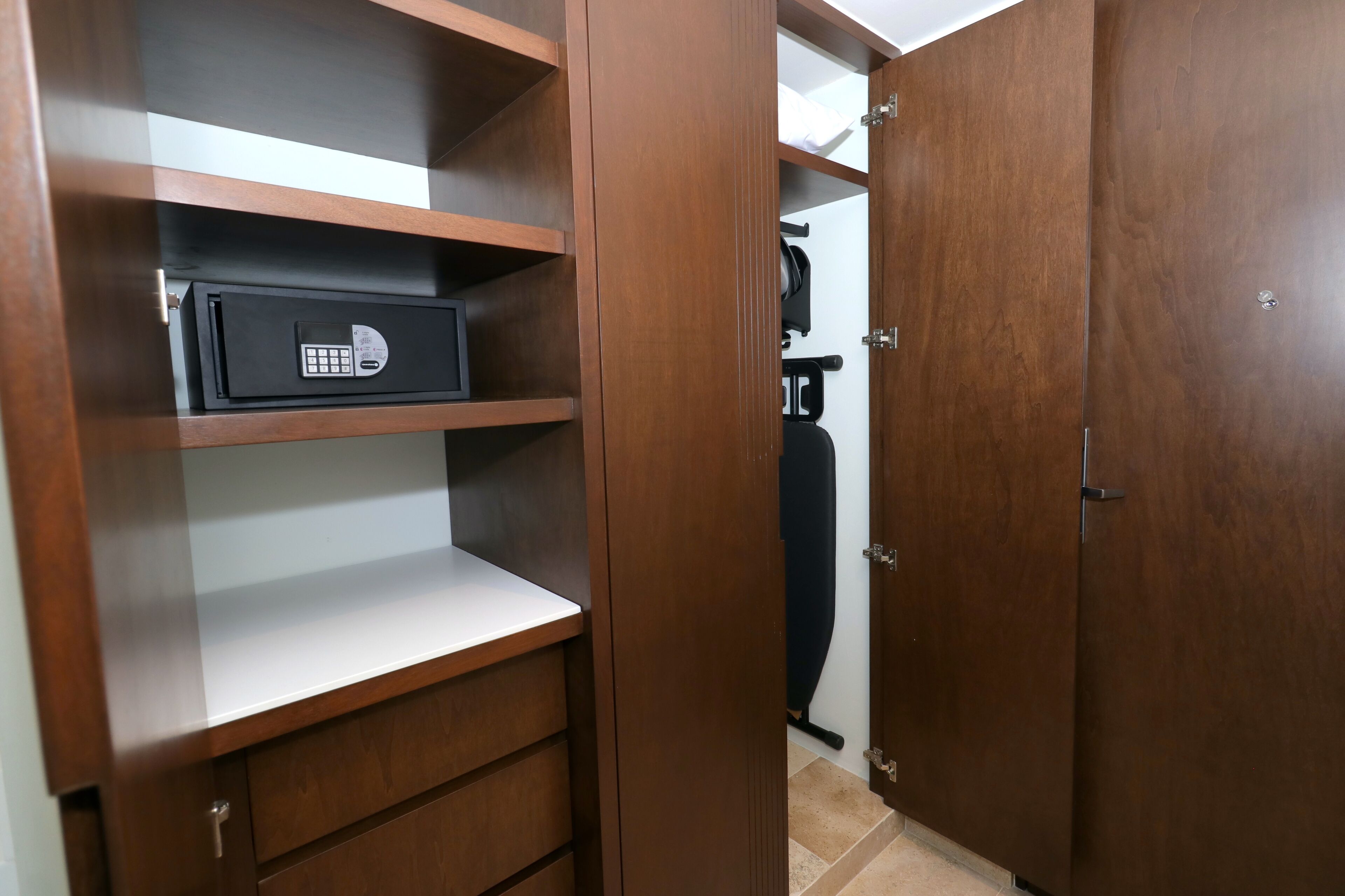 A wooden wardrobe with a built-in safe, a mirror, and a hanging coat.