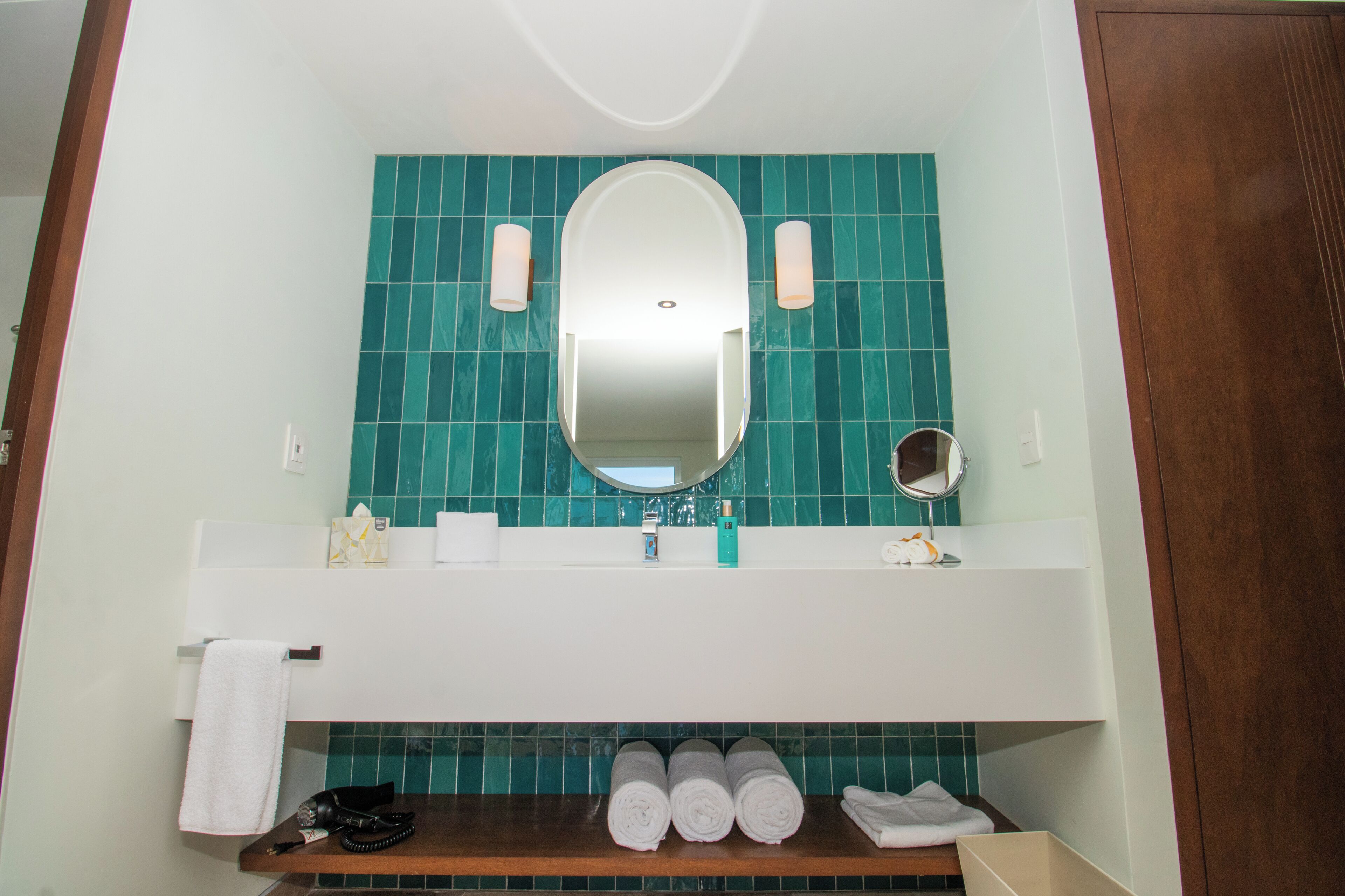 Ein Badezimmer mit Spiegel, Waschbecken, Handtuchhalter und Ablagefläche mit gerollten Handtüchern.