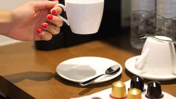 Una mano sosteniendo una taza blanca, un plato con una cuchara y condimentos sobre una mesa.