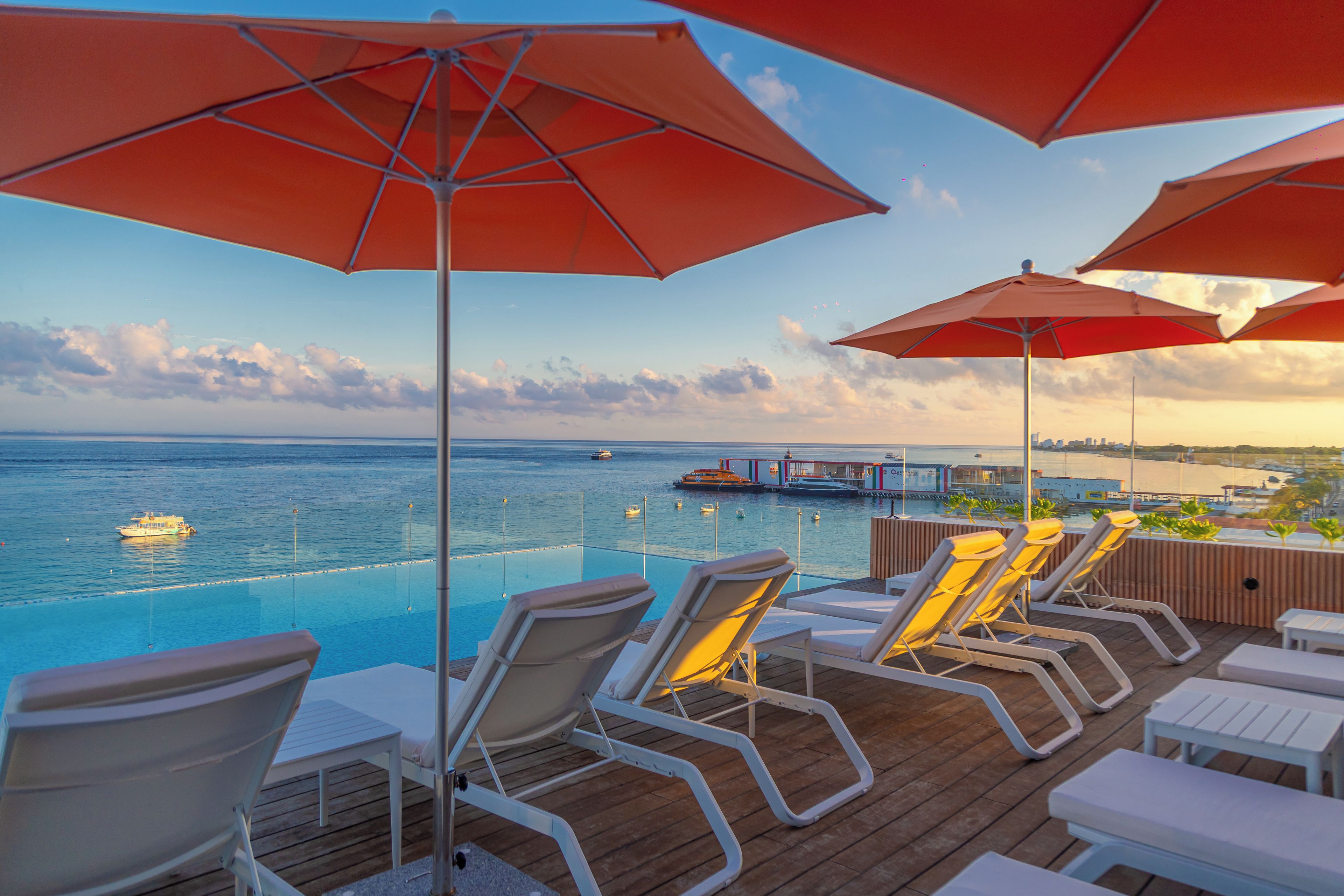 A poolside area with lounge chairs and umbrellas, overlooking a body of water with boats.