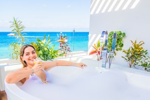 A person in a bathtub with a view of the ocean and plants. - Hotel Casa Bahía Cozumel - Adults Only (Cozumel)