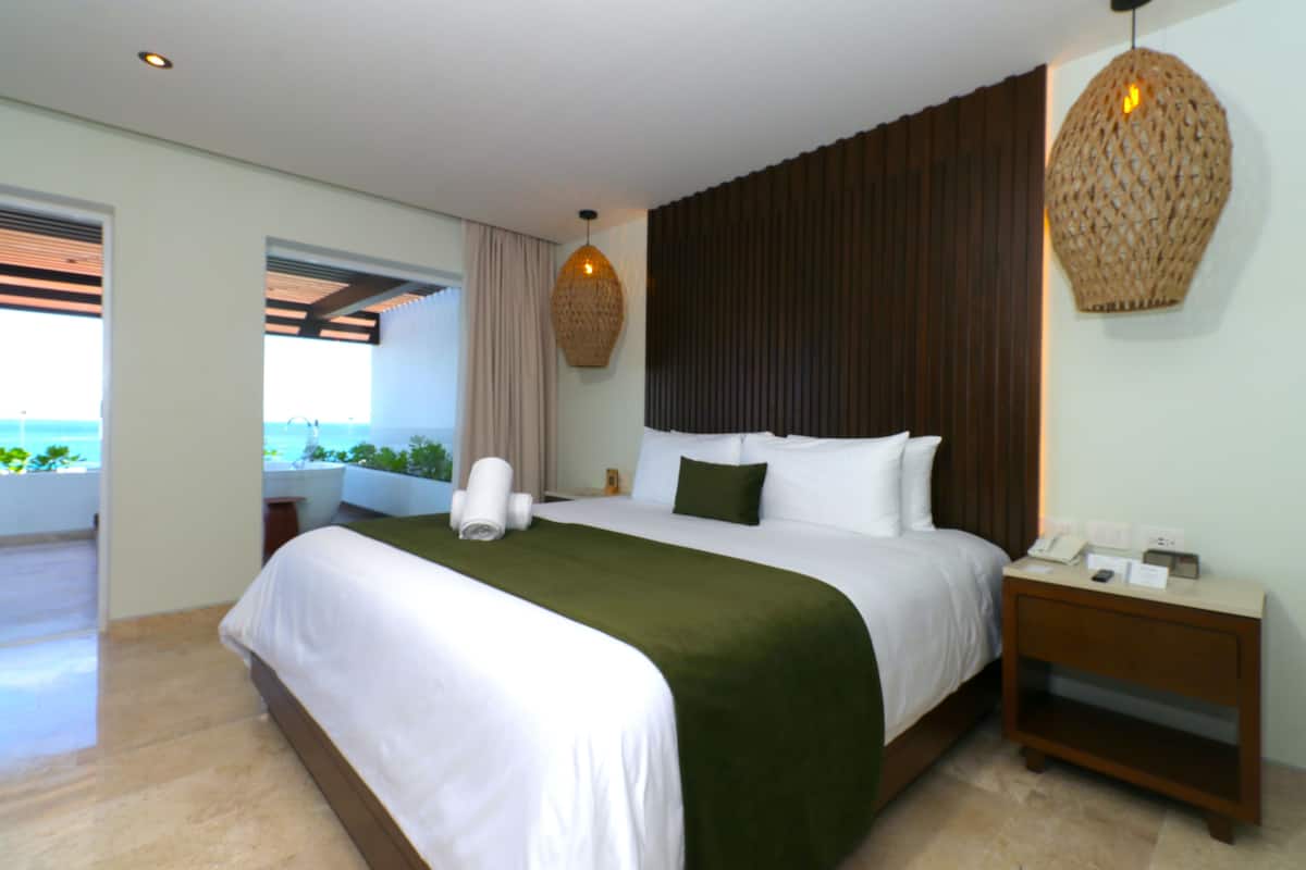 Habitación de hotel con una cama grande, una mesita de noche, una lámpara colgante y vistas al exterior.