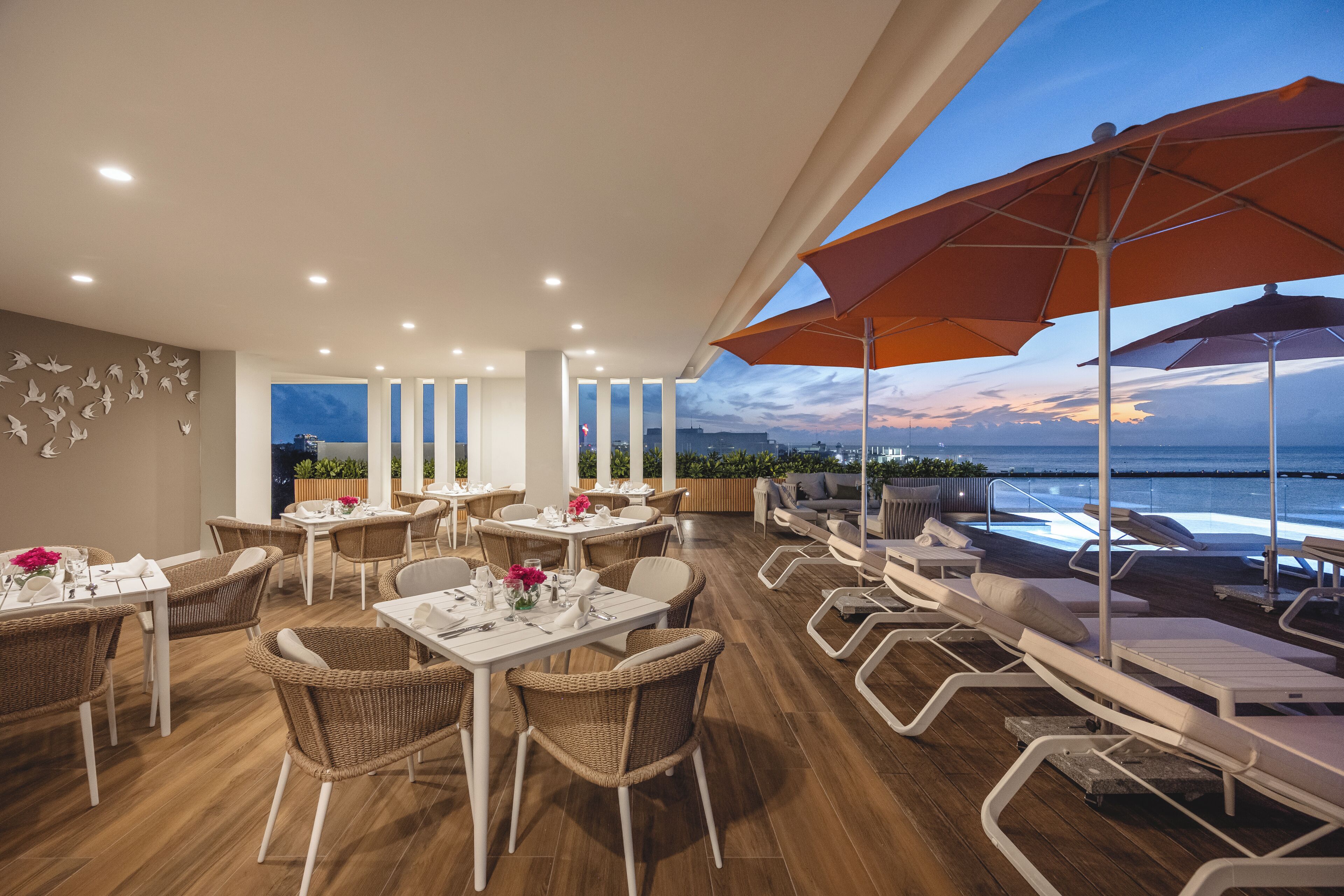 A restaurant with tables and chairs, a view of the ocean, and a sunset.
