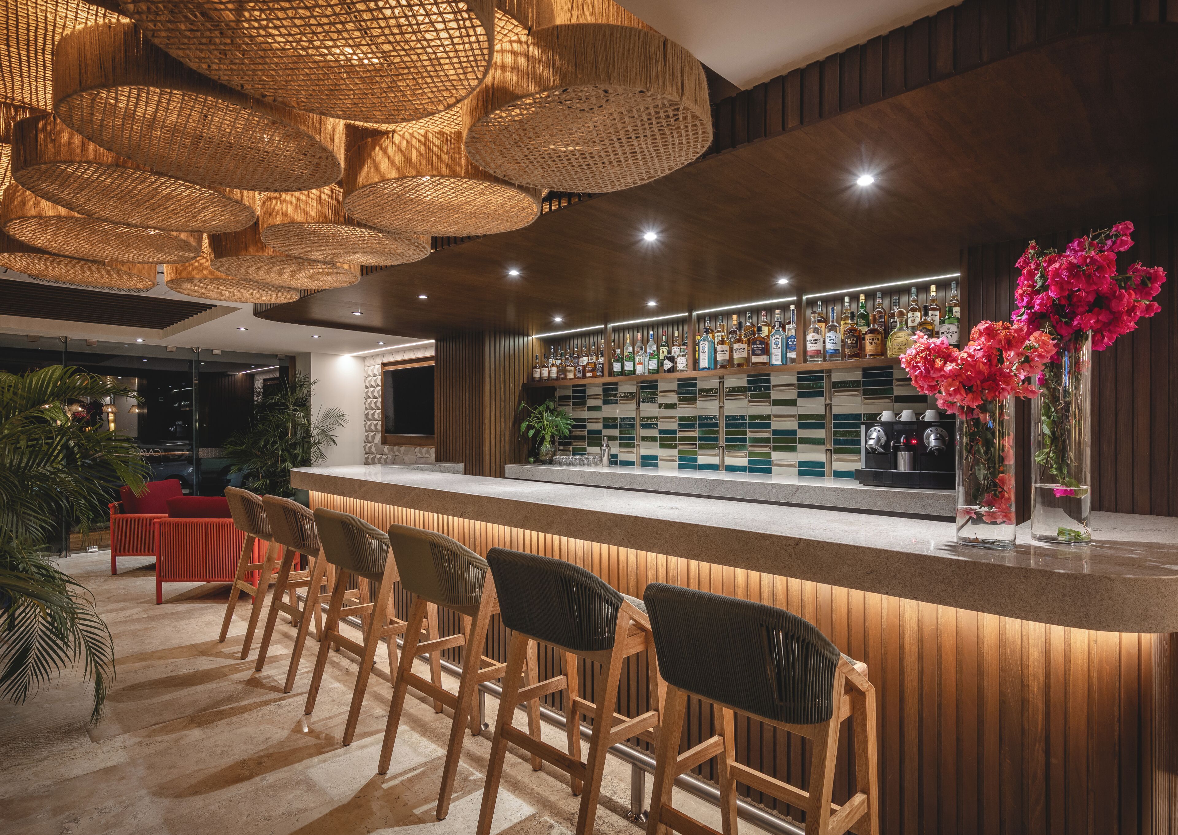A bar area with wooden chairs, a counter with bottles, and hanging wicker lamps.