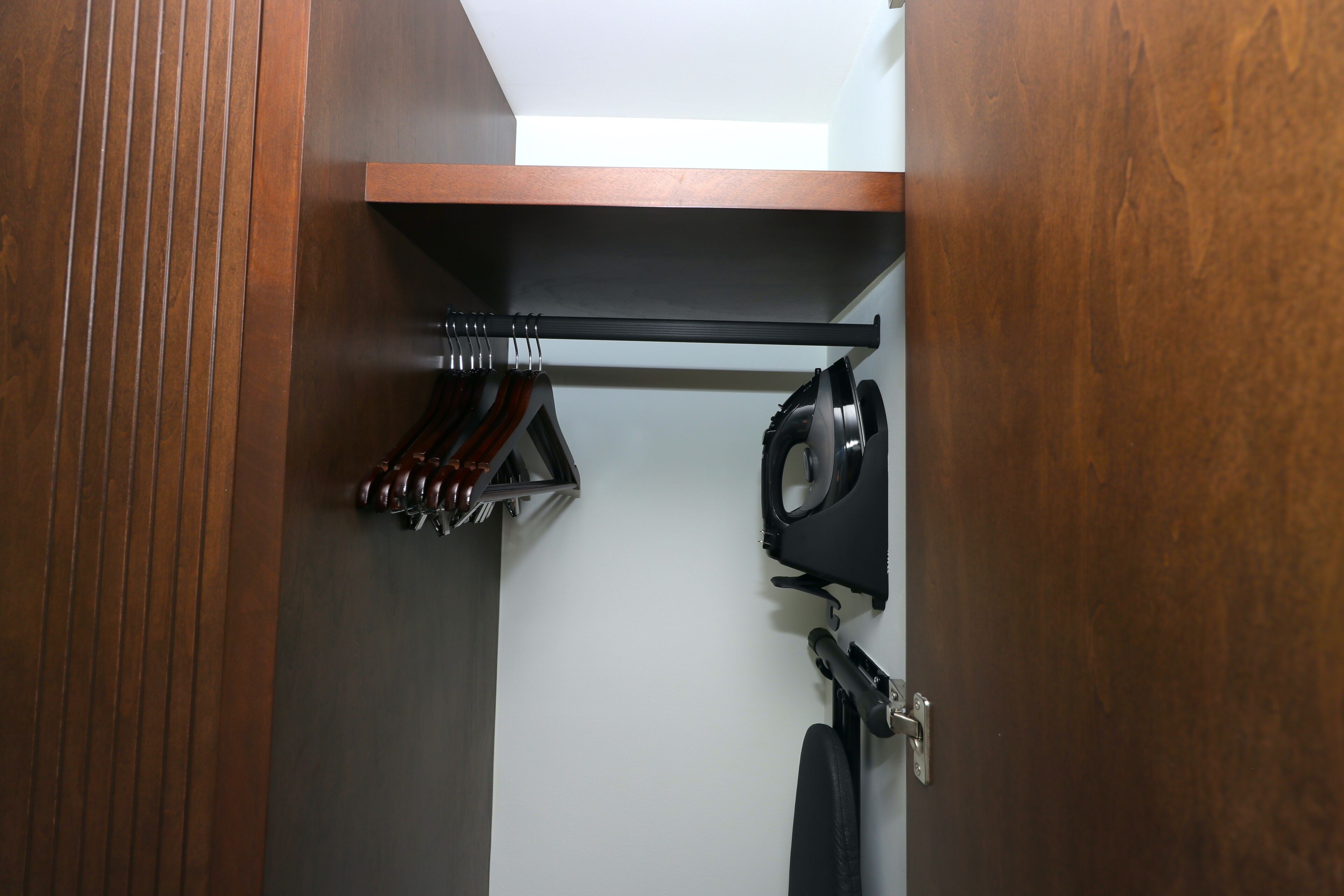 A closet with wooden doors, a black coat rack, and a black chair.