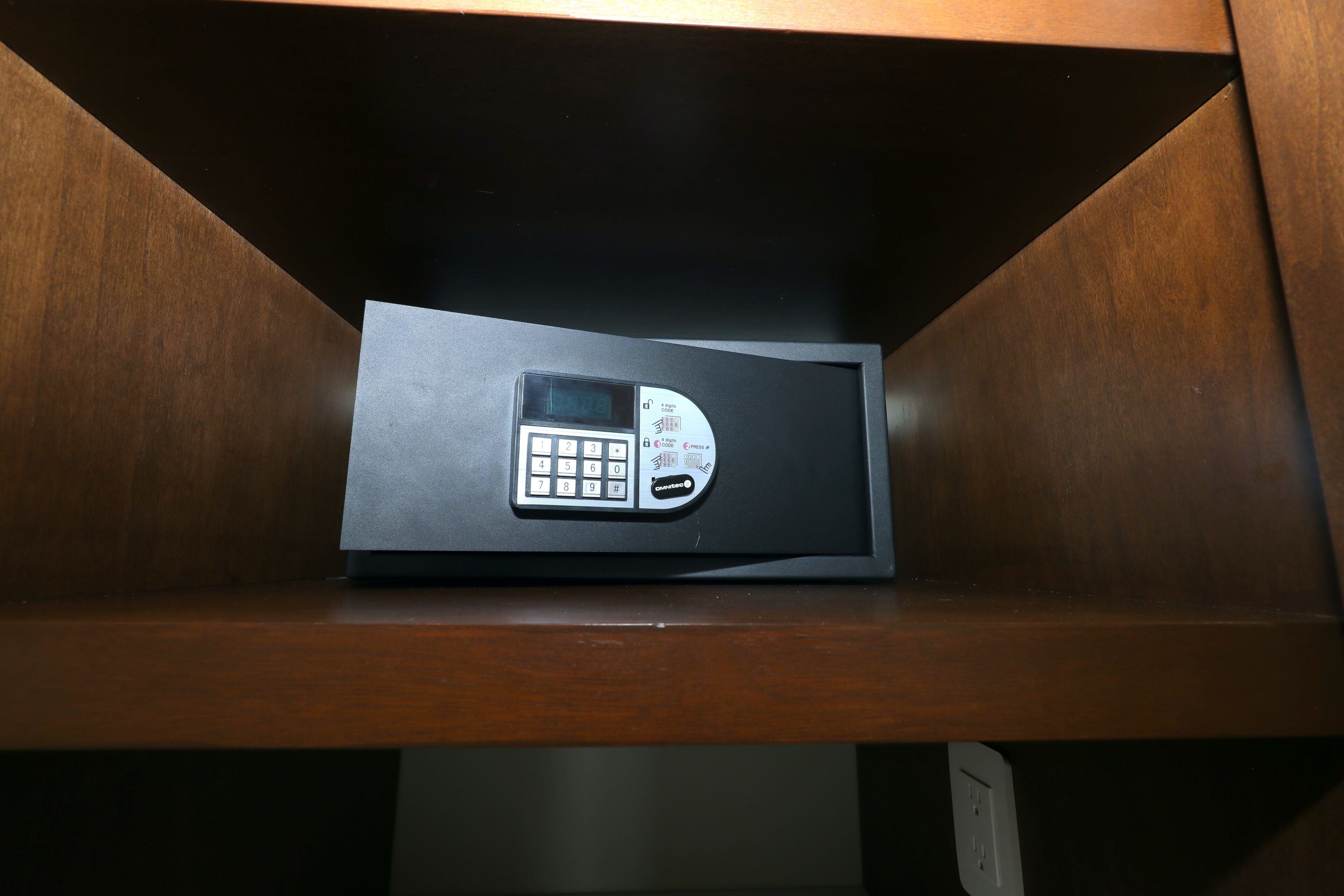 A safe deposit box with a keypad, located in a wooden cabinet.