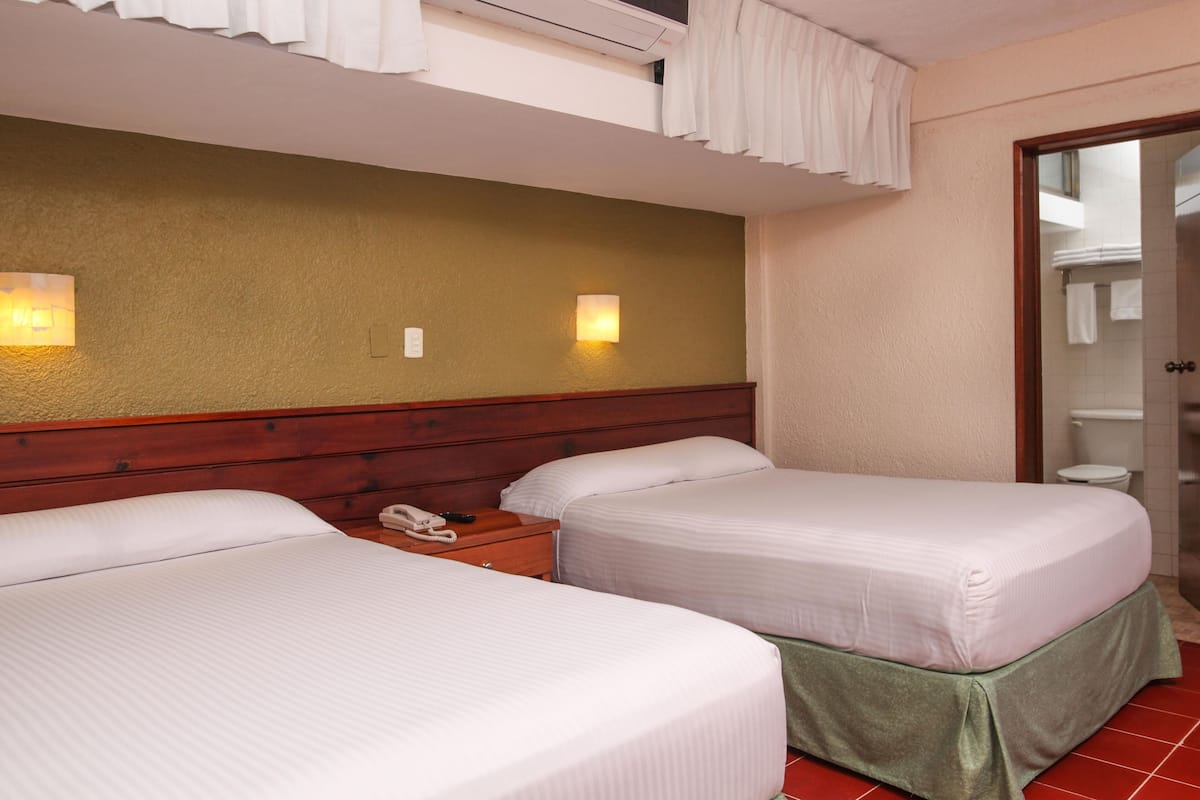 A hotel room with two beds, a wooden headboard, a bedside table with a phone, and a bathroom visible through an open door.