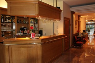 Een bar met een houten toonbank, planken met flessen en glazen, en een zithoek met stoelen en een tafel.