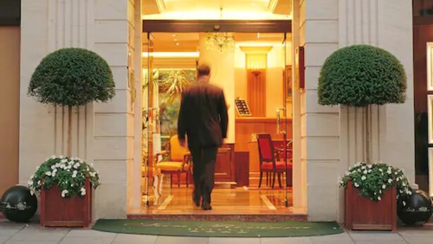 L’entrée de l’hôtel Sun Riviera, avec une enseigne bien visible au-dessus de la porte, un homme qui entre, et deux plantes en pot de chaque côté.