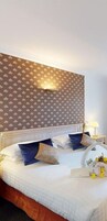 Een net opgemaakt bed met een gestreept hoofdbord, een nachtkastje met een lamp en een klein decoratief object erop.