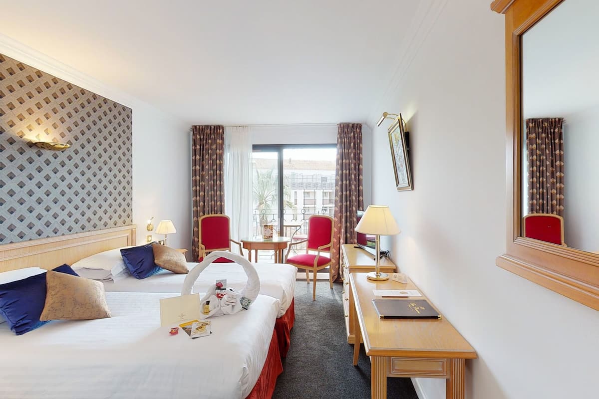 A hotel room with two beds, a desk, chairs, and a large mirror.
