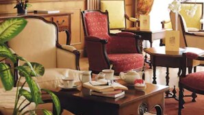 Une pièce avec un canapé beige, un fauteuil rouge, une table basse en bois et un vase rempli de fleurs.