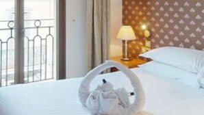 Une chambre d’hôtel avec un lit, une table de chevet avec une lampe, une fenêtre donnant sur des immeubles et un rideau.