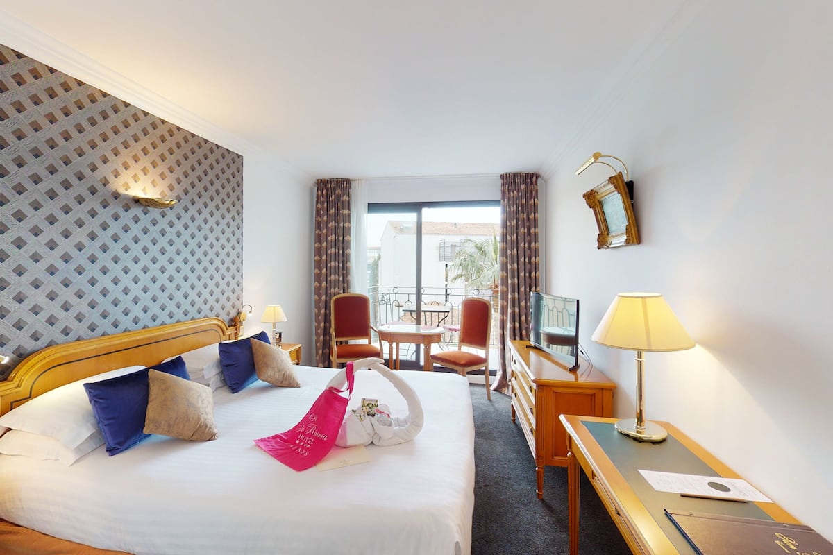 A hotel room with a bed, two chairs, a table, a desk, a TV, and a window with curtains.