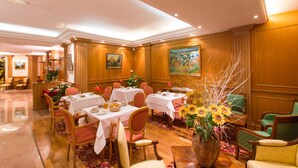 Une salle à manger d’hôtel avec des tables préparées pour le petit-déjeuner, un lambris en bois et un grand vase rempli de tournesols.