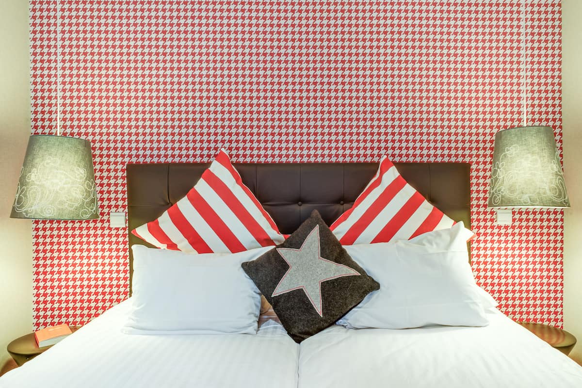A bed with white and red striped pillows, a gray star-shaped pillow, and a red and white striped pillow.