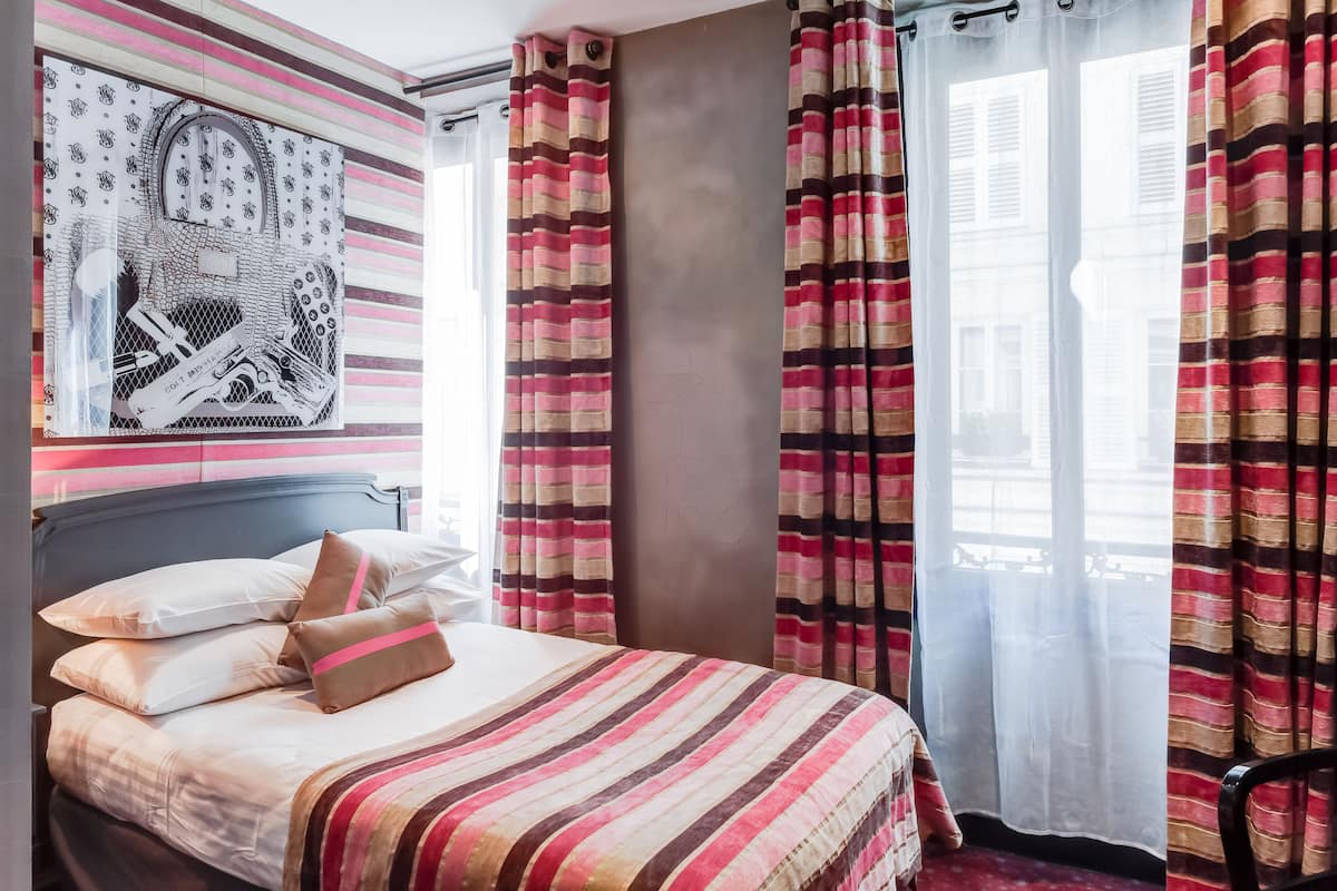 A hotel room with a bed, pillows, a wall art piece, and striped curtains.
