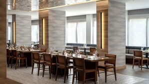 A modern dining area with multiple tables and chairs, large windows, and a high ceiling with decorative lighting. - Austin Marriott South (Austin)