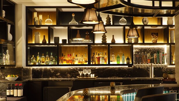 A bar area with shelves of bottles, a marble countertop, and hanging lamps. - Austin Marriott South (Austin)