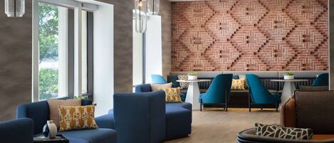 A modern lounge area with blue sofas, a brick-patterned wall, and pendant lighting.