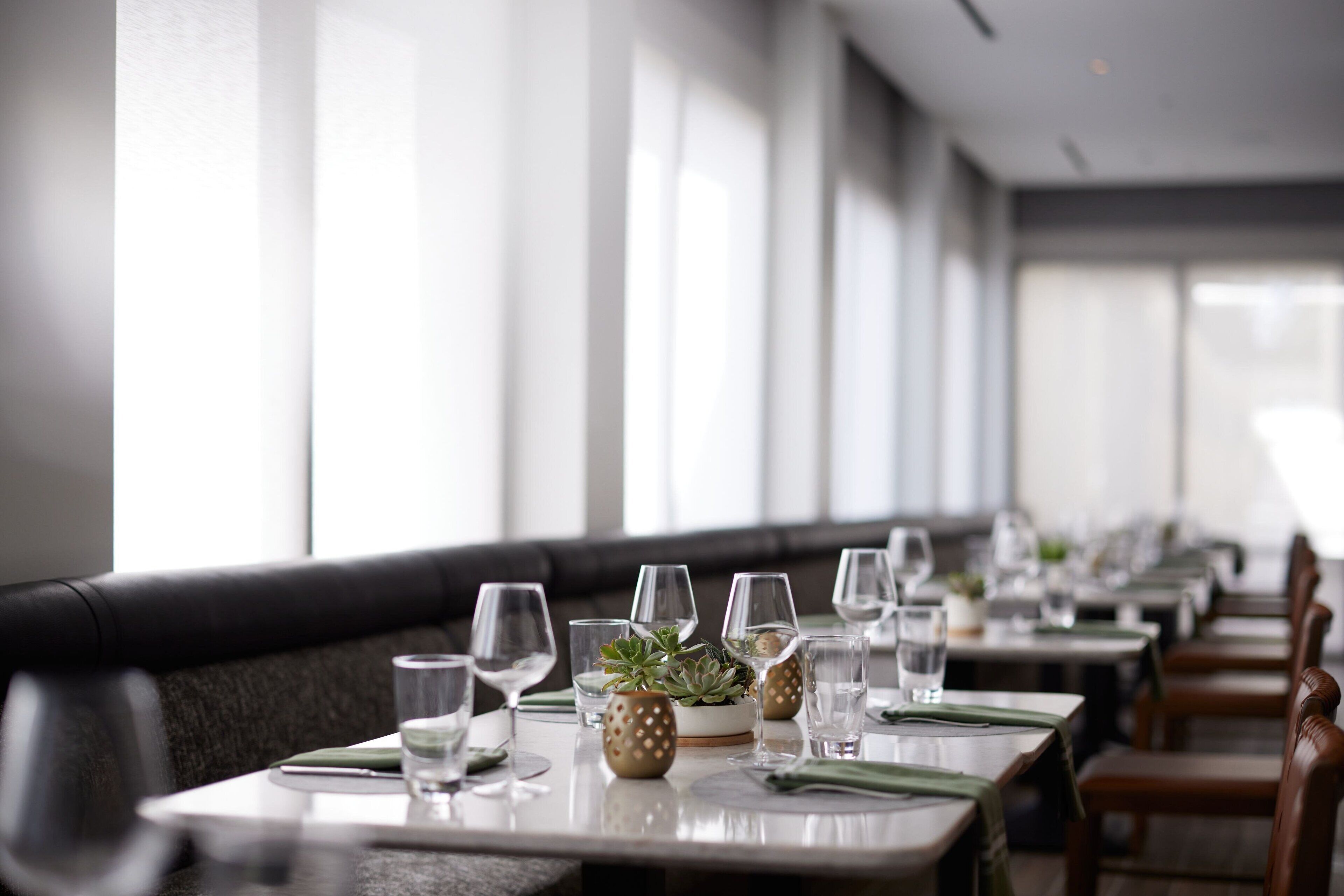 A restaurant with long tables set for dining, each with a water glass, a small plant, and a napkin.