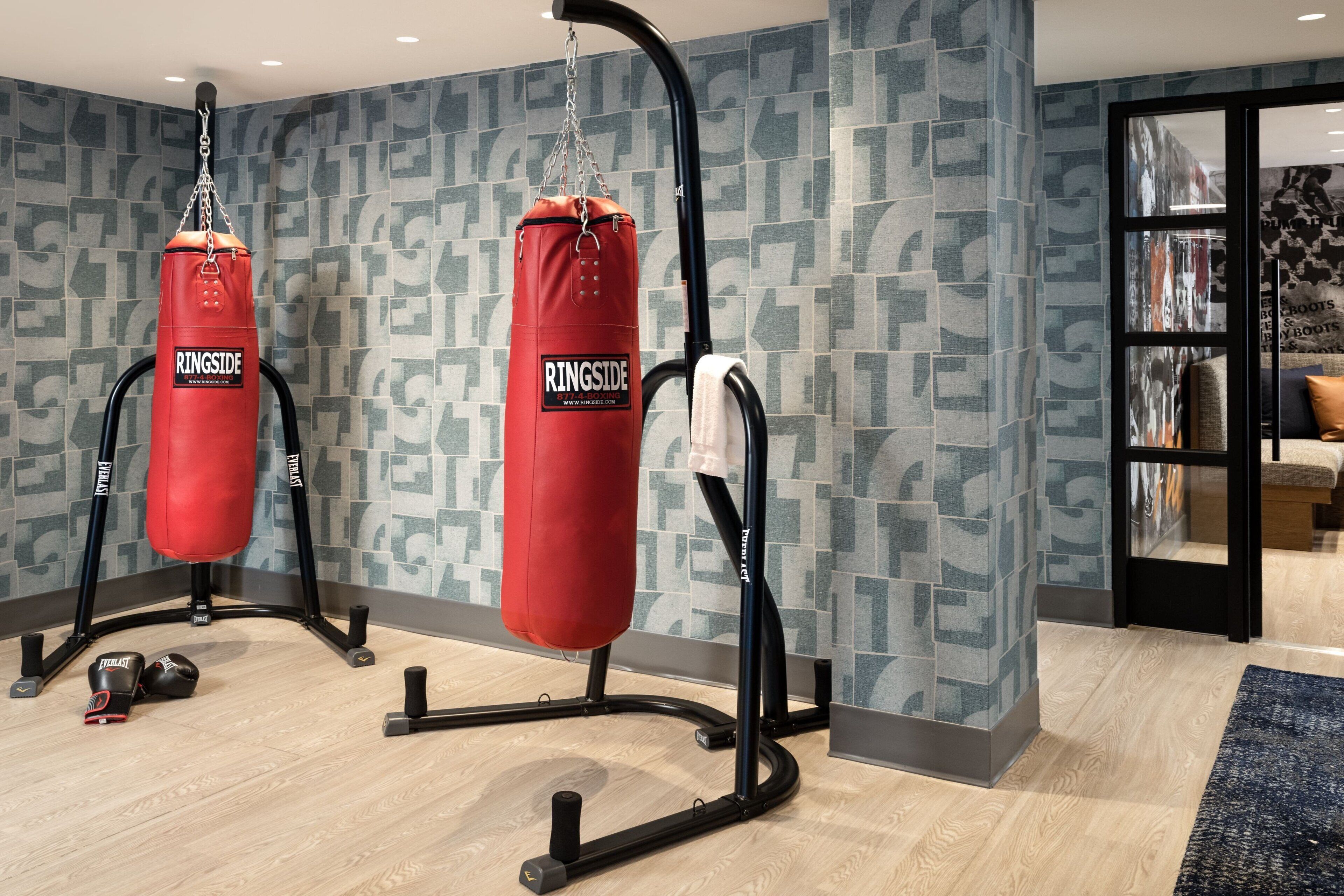 Un gimnasio en casa con dos sacos de boxeo rojos, piso de madera y pared con diseño.