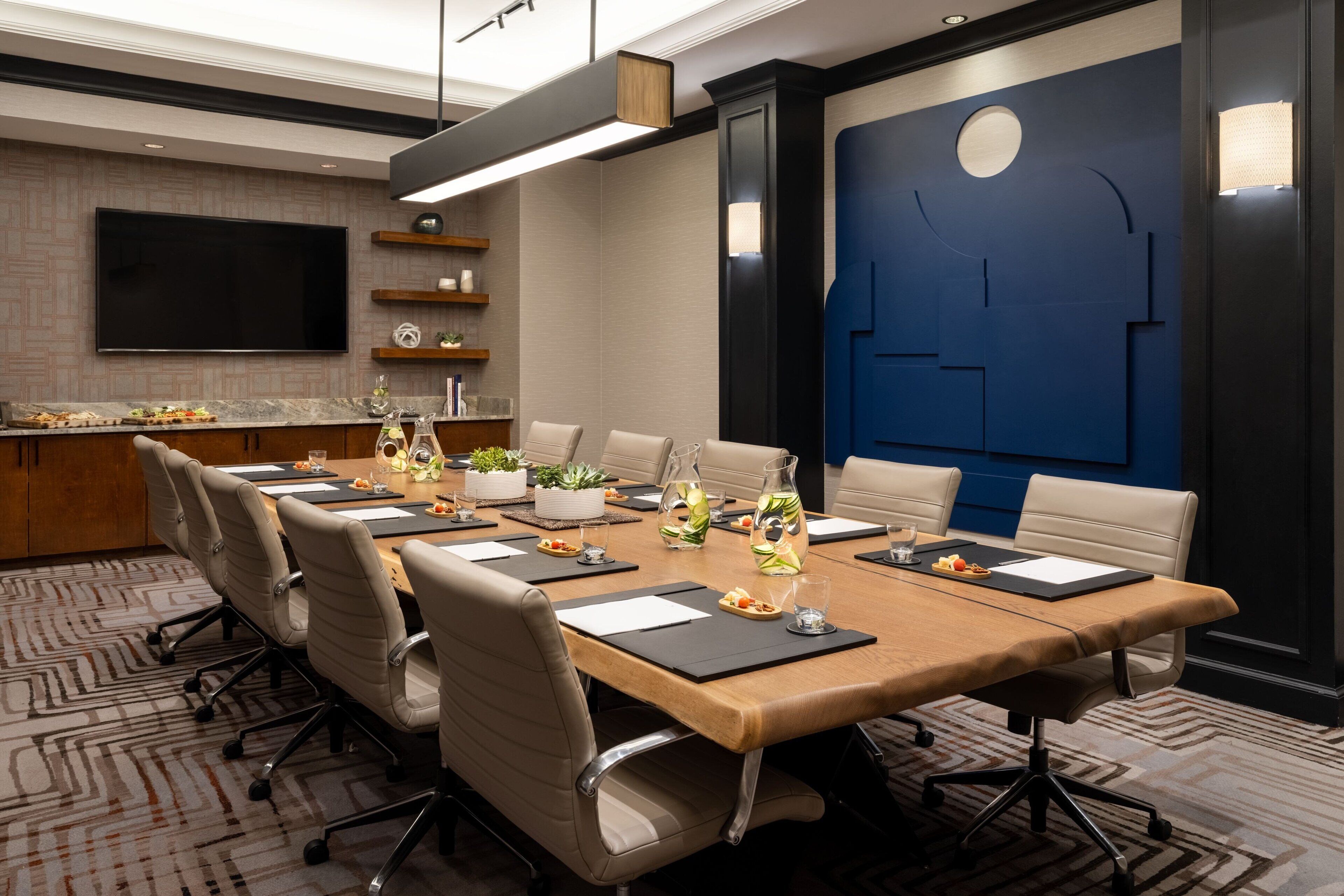 A conference room with a long table, chairs, a TV, and a blue accent wall.