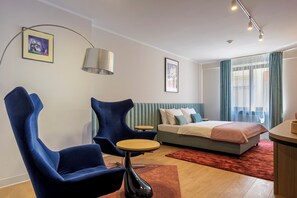 Ein modernes Hotelzimmer mit Bett, zwei Stühlen, einem kleinen Tisch, einer Lampe und Kunstwerken an den Wänden.