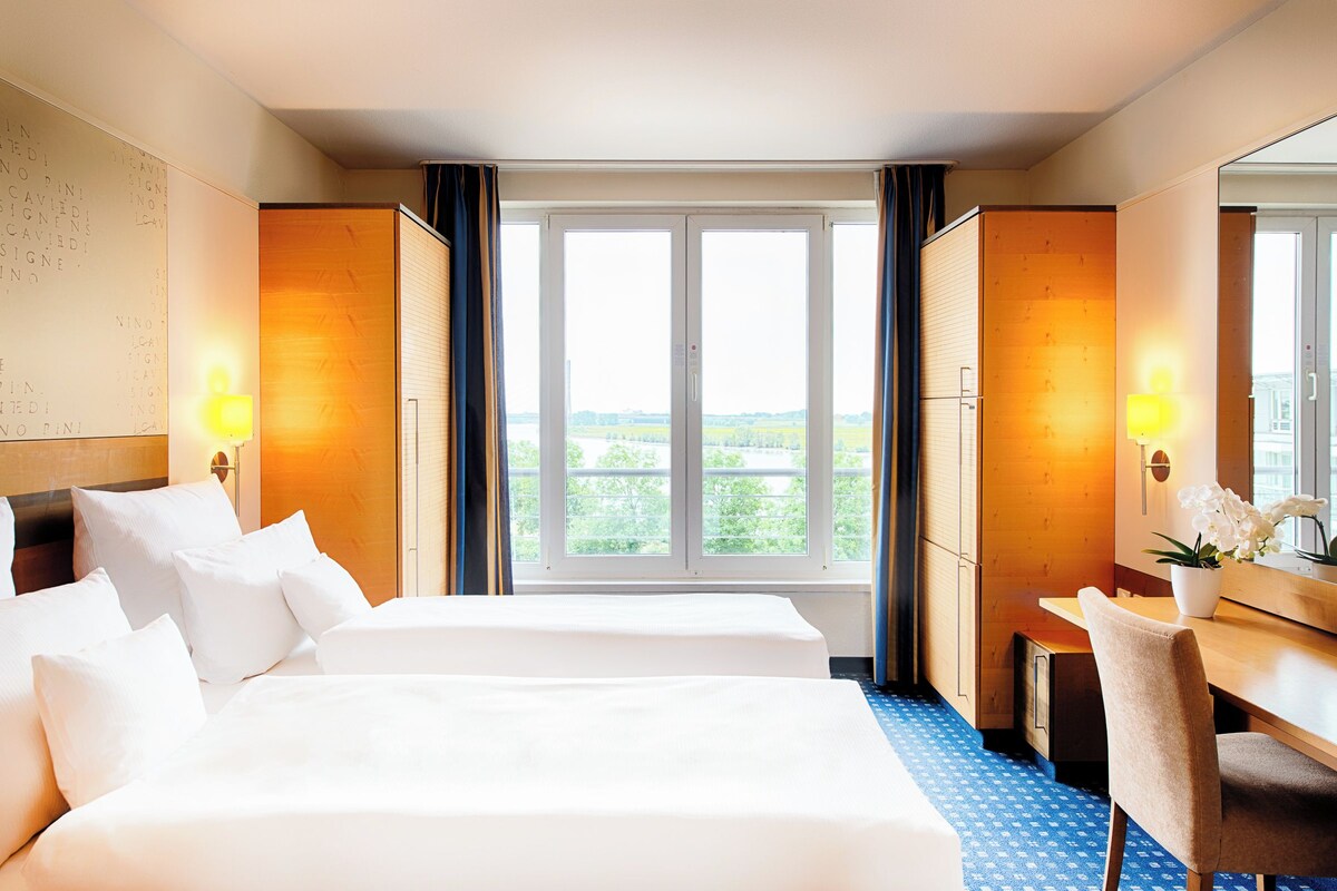 Een hotelkamer met twee bedden, een bureau en een groot raam met uitzicht.