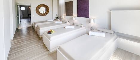 A modern hotel room with three beds, a large mirror, and a chandelier.