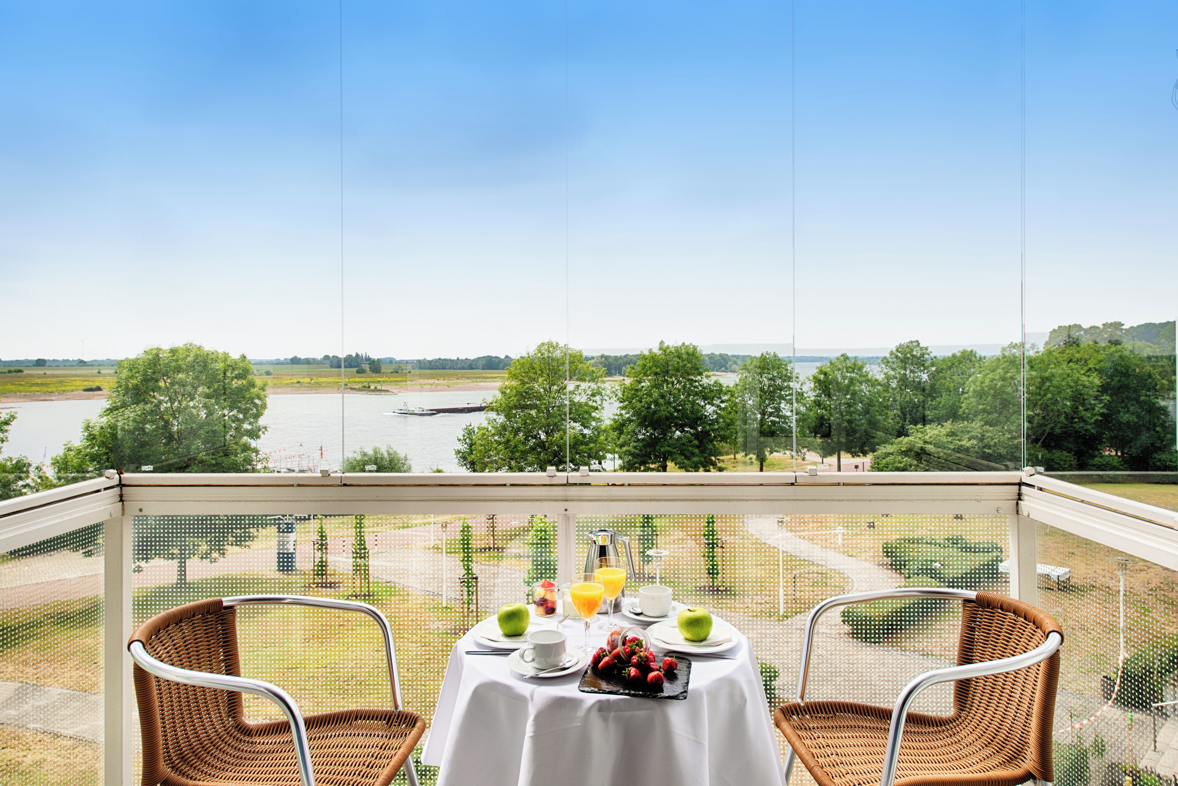 Ein Balkon mit einem Tisch für zwei Personen, mit Blick auf einen Fluss und grüne Vegetation.