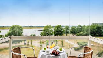 Ein Balkon mit einem Tisch für zwei Personen, mit Blick auf einen Fluss und grüne Vegetation.