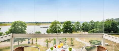 A balcony with a table set for two, overlooking a river and greenery.