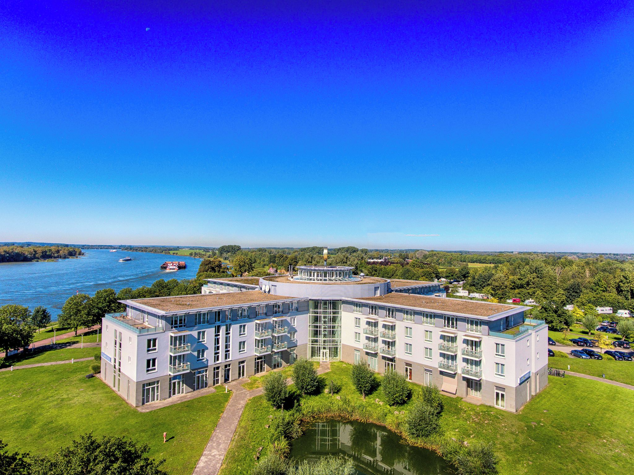 A modern hotel with a central courtyard, surrounded by lush greenery and a body of water.