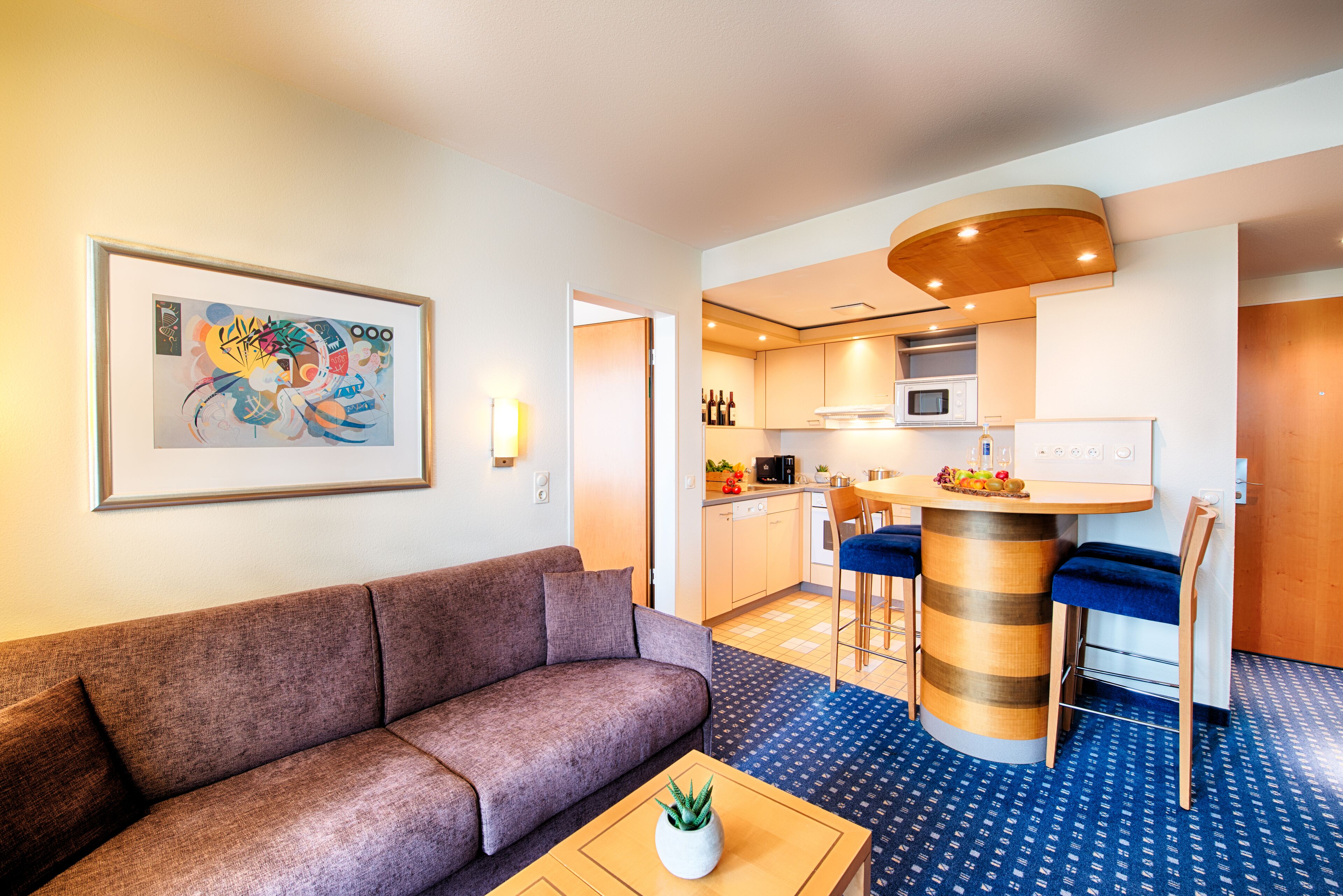 Een moderne woonkamer met een bank, een bijzettafeltje met een plant, en een keuken met een bar en krukken.