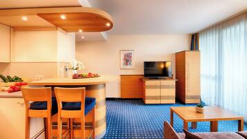 Habitación de hotel compacta con kitchenette, zona de comedor con dos sillas, un televisor pequeño y un ventanal grande con cortinas.
