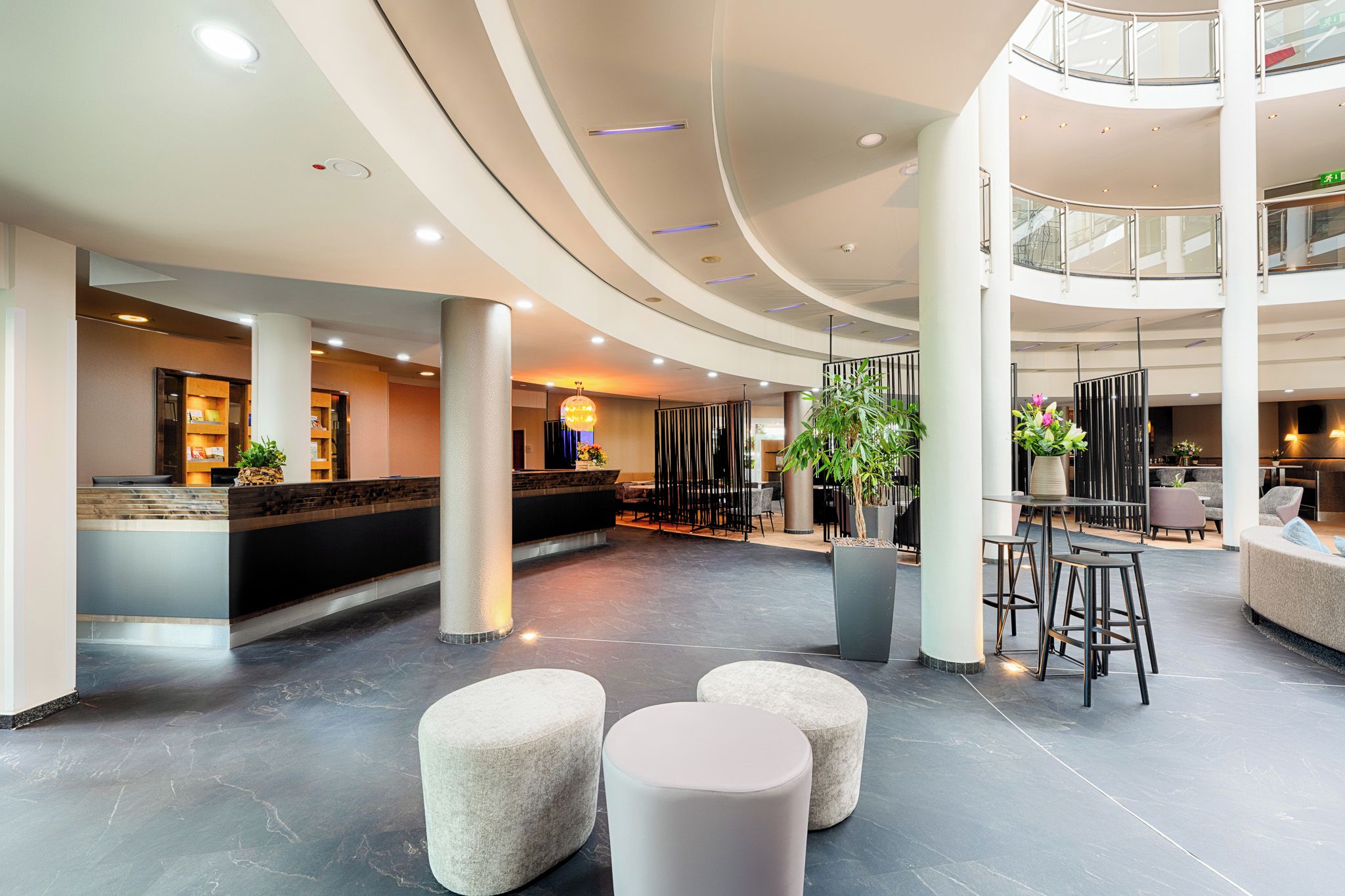 A modern hotel lobby with a reception desk, seating areas, and a staircase leading to an upper level.