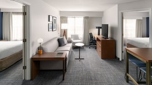 A hotel room with a bed, a sofa, a desk, a chair, a TV, and a lamp.