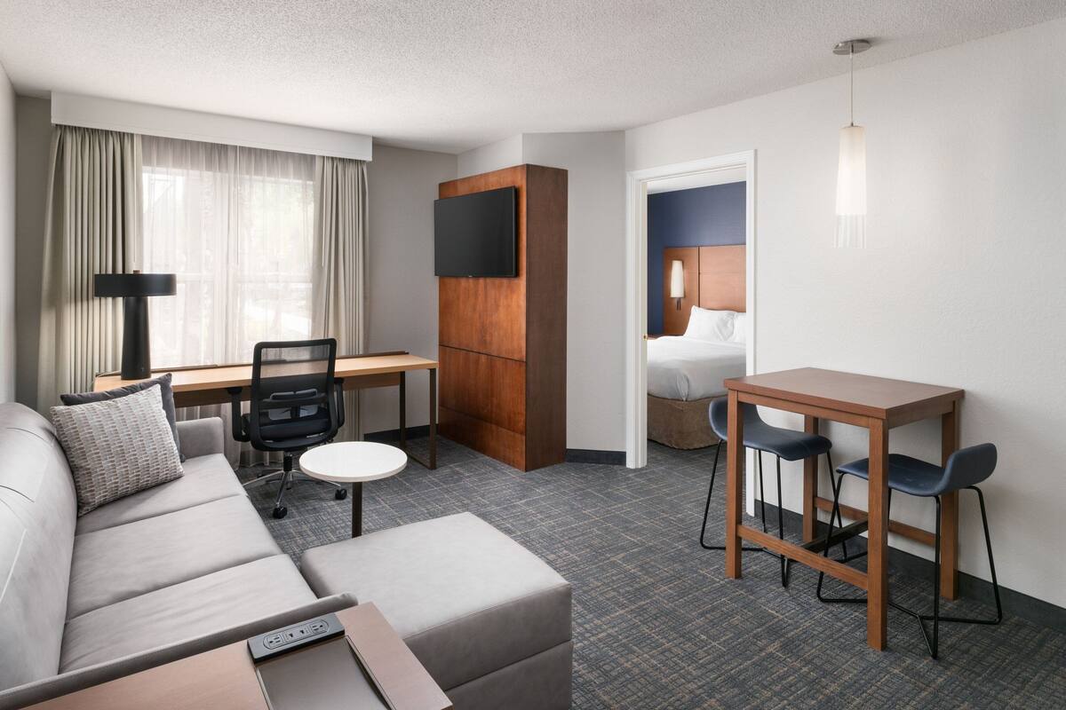 A hotel room with a sofa, a desk, a chair, a TV, and a bed.