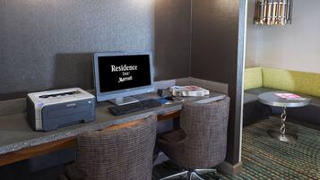 A hotel room with a desk, a Brother printer, a Brother scanner, a Brother keyboard, a Brother monitor, and a small round table with a magazine.