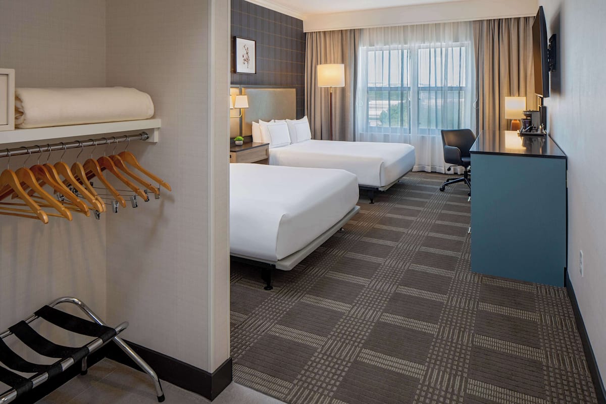 A hotel room with two beds, a desk, a chair, a TV, and a wardrobe with hangers.