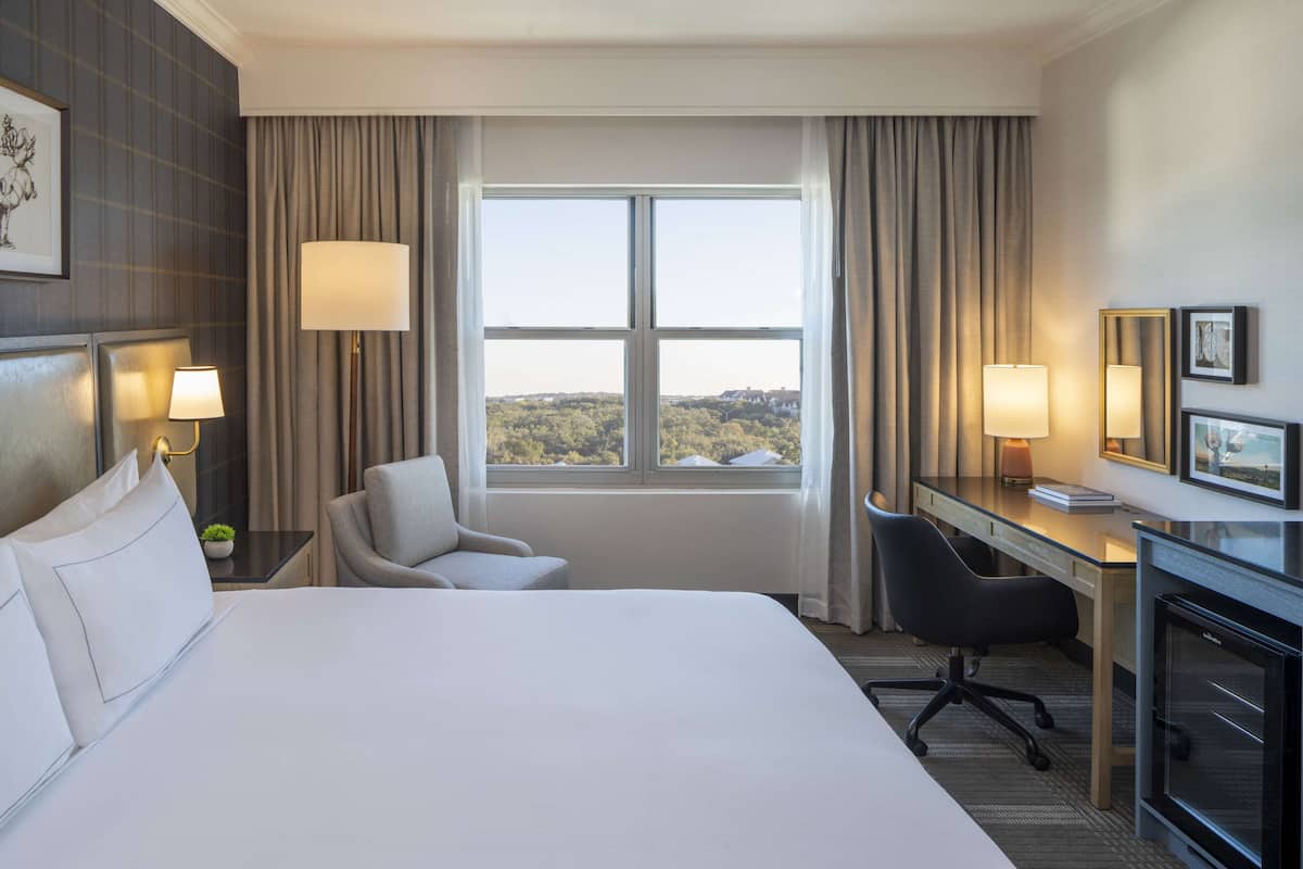 A hotel room with a large bed, a desk, a chair, and a view of the outdoors through a window.