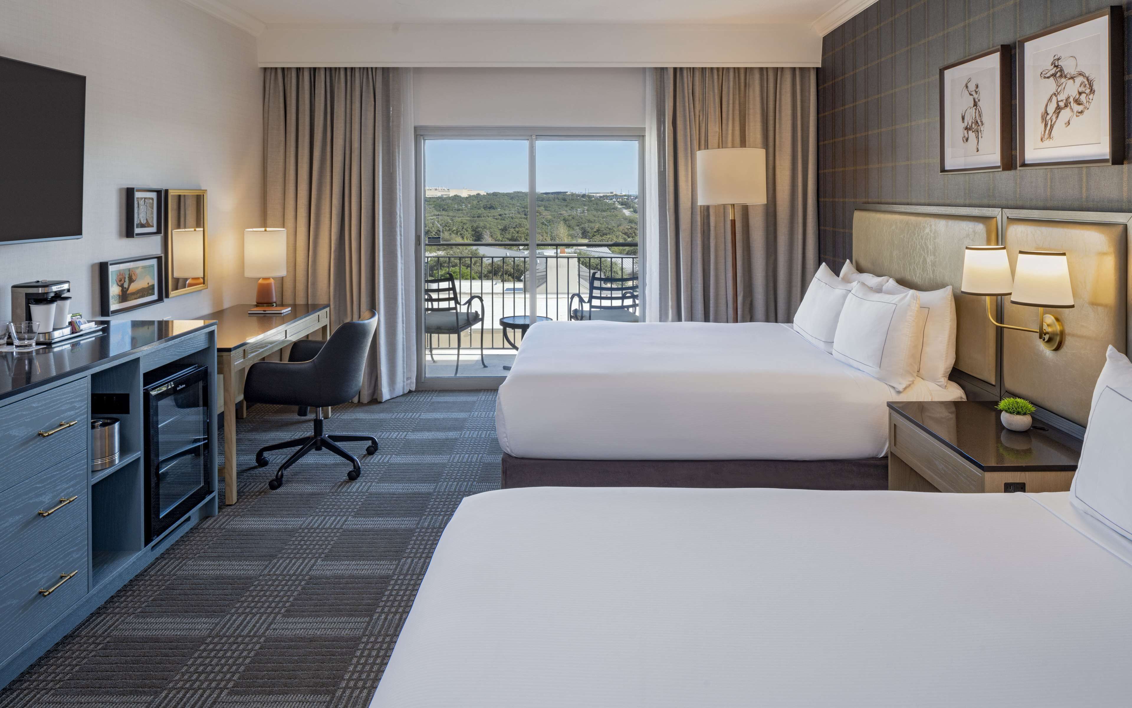 Une chambre d’hôtel avec deux lits, un bureau, une chaise, une télévision et un balcon avec vue.
